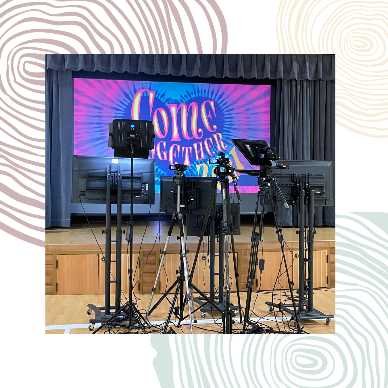 A set of cameras and monitors face a stage with a large colorful screen, designed in Canva, displaying the words "Come Together 2023.