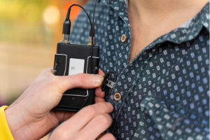 Image shows two hands clipping a lav mic onto someone's shirt button