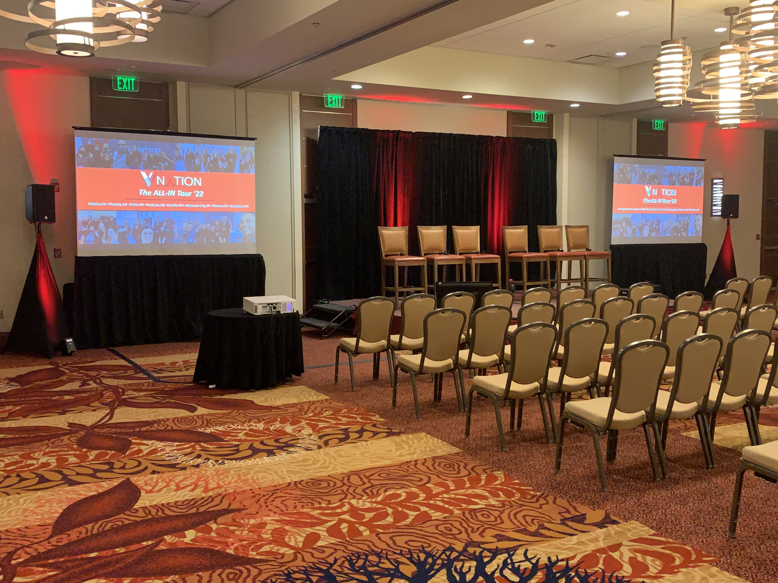 IMG_4876 Conference room setup with rows of chairs facing a stage, four chairs, dual projector screens displaying slides, and red lighting accents—ideal for corporate events using Seattle AV services for conferences.