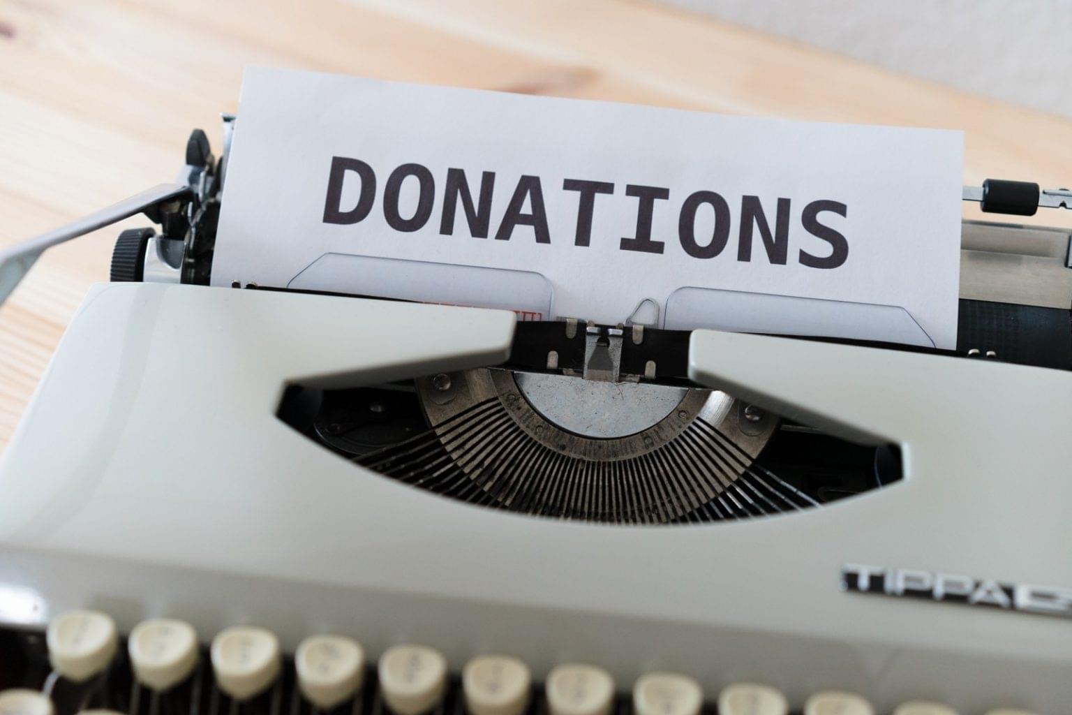 A sheet of paper with the word "DONATIONS" typed on it is inserted into a vintage typewriter on a wooden surface, highlighting support for nonprofits and schools.