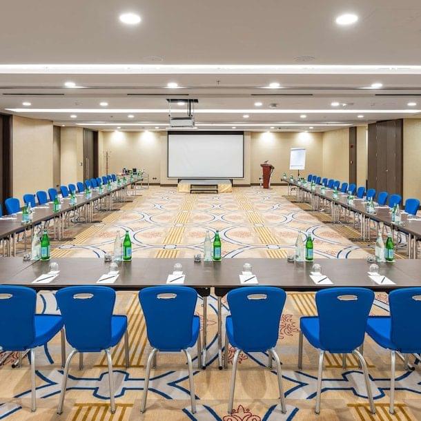 Conference room with U-shaped tables set with water bottles, notepads, and pens; blue chairs surround the tables, and a projector screen at the front is ready for Seattle AV Services for Hotels and Venues.