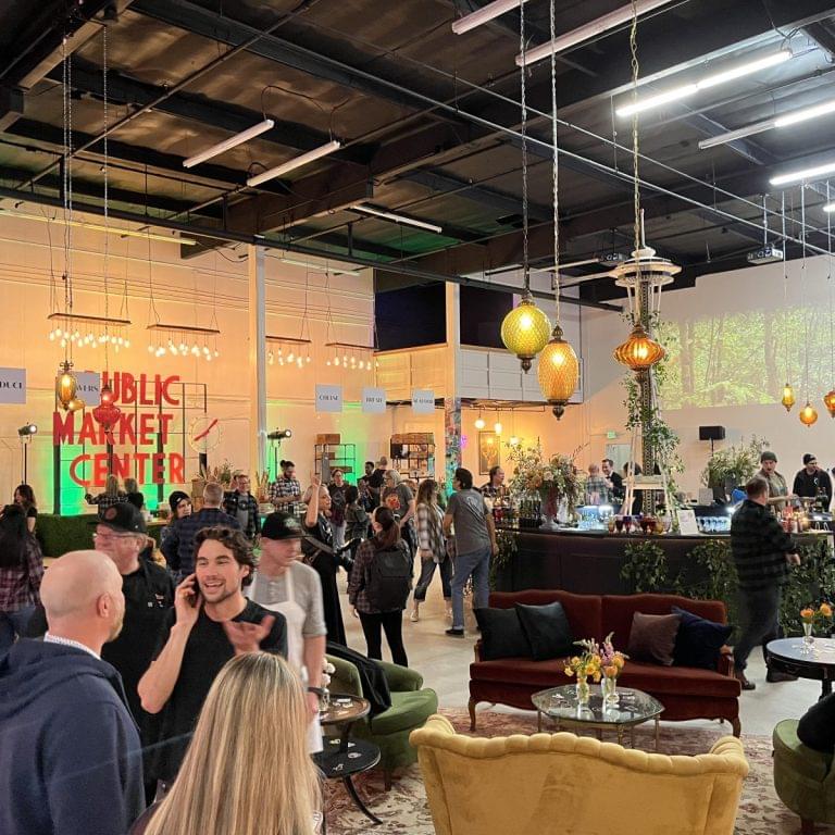 People gather at an indoor event space with lounge seating, decorative lights, and a market-style atmosphere. Seattle AV services for corporate events and conferences enhance the experience as guests mingle and explore various booths and displays.