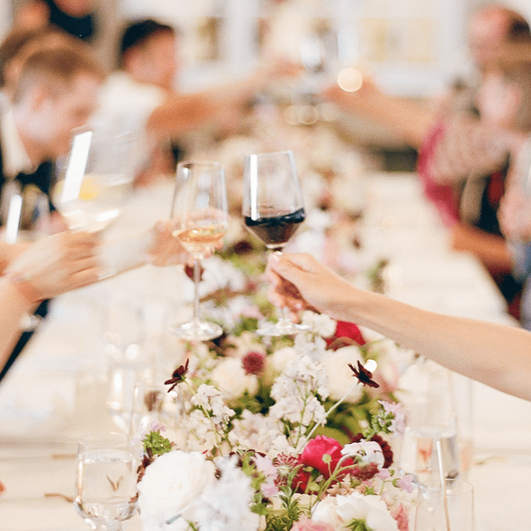 People seated at a long table raise their wine glasses in a toast, with floral arrangements running down the center—perfect for Seattle weddings and private events enhanced by professional AV services.
