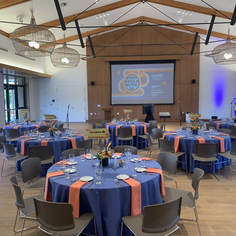 Conferences second image A banquet hall with round tables covered in blue and orange tablecloths, set for an event, features a stage, podiums, and a presentation screen—ideal for those seeking Seattle AV services for corporate events and conferences.