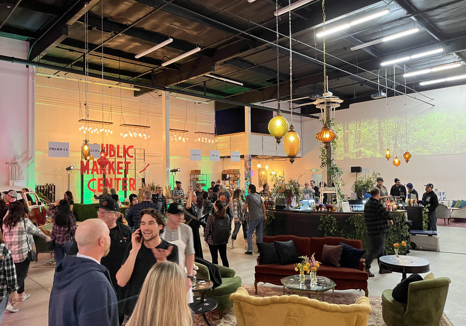 People gather at an indoor event space with lounge seating, decorative lights, and a market-style atmosphere. Seattle AV services for corporate events and conferences enhance the experience as guests mingle and explore various booths and displays.