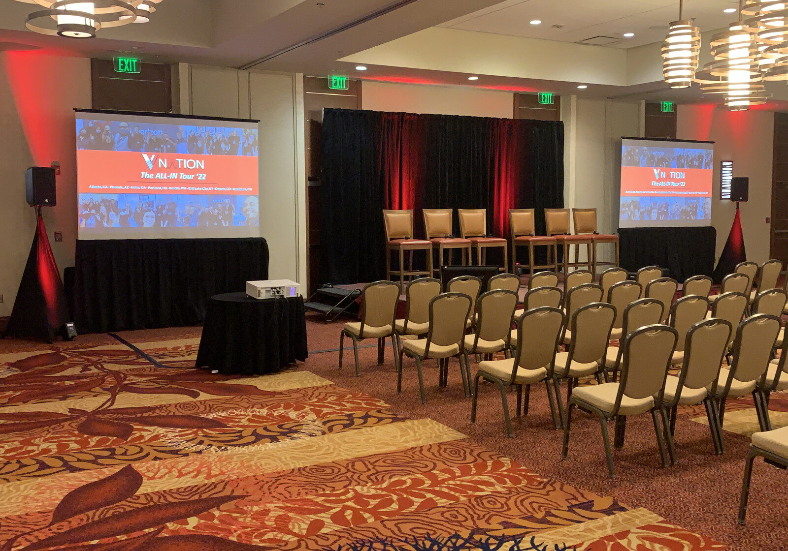 Conference room setup with rows of chairs facing a stage, four chairs, dual projector screens displaying slides, and red lighting accents—ideal for corporate events using Seattle AV services for conferences.