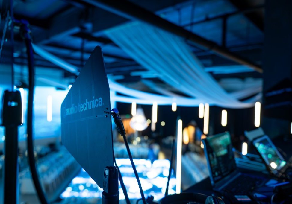 Audio-Technica microphone setup in a dimly lit, modern event space with blue lighting and various equipment, showcasing comprehensive audio visual event services for all occasions.