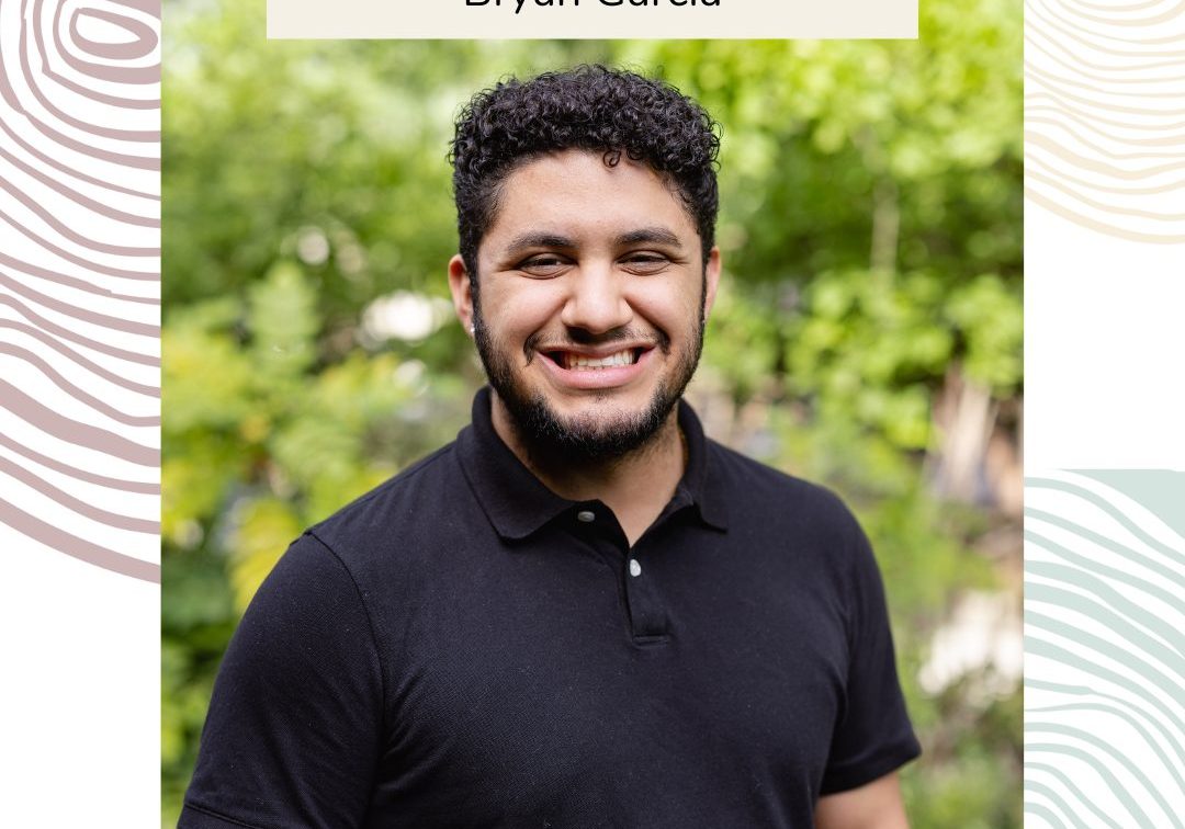 A man with curly hair and a beard, wearing a black polo shirt, smiles outdoors in front of green foliage. Text above reads "Bryan Garcia," highlighting his drive and passion for his audiovisual career.