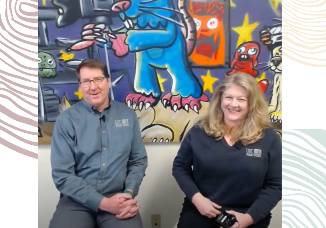 Dave and Jennifer sit in front of a wall mural while being interviewed.
