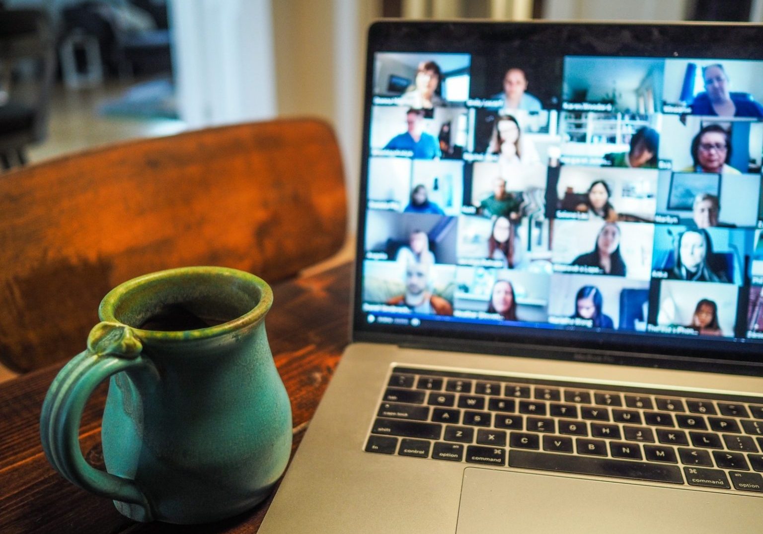 A ceramic mug sits on a wooden table next to a laptop displaying a virtual meeting, perfect for those who create virtual content and connect with colleagues online.