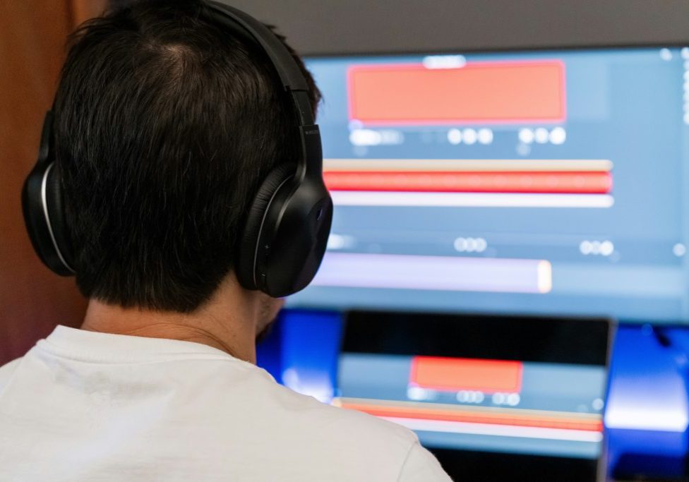 fellipe-ditadi-VlL2_DY8Vns-unsplash Person wearing headphones sits in front of a computer monitor displaying colorful charts and graphs on the screen.
