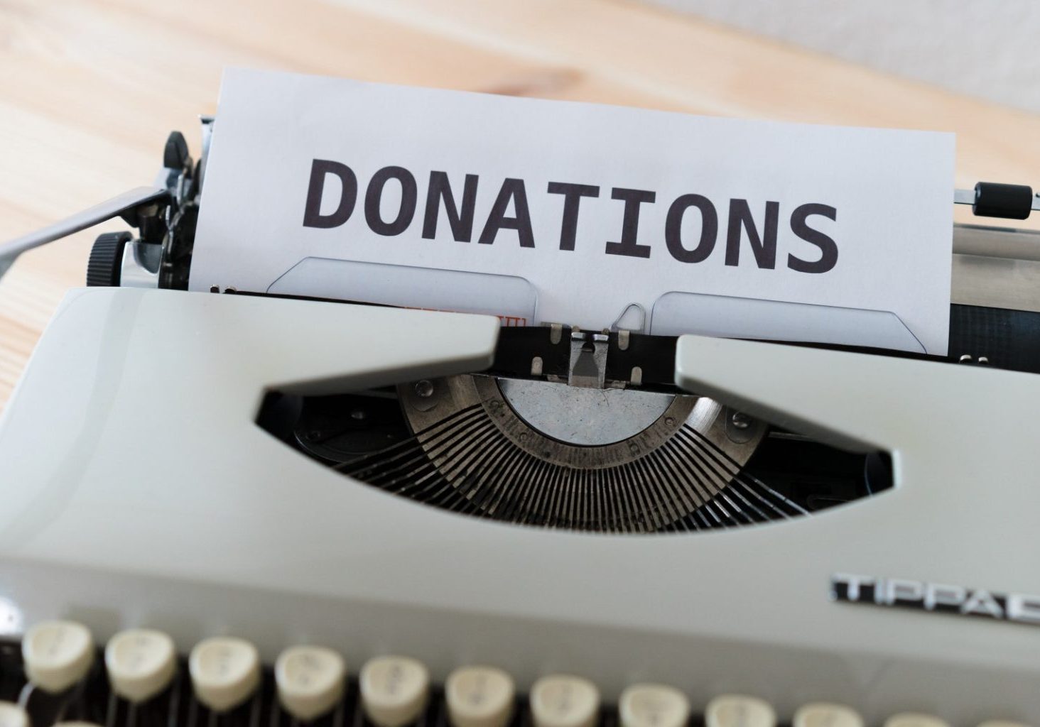 A sheet of paper with the word "DONATIONS" typed on it is inserted into a vintage typewriter on a wooden surface, highlighting support for nonprofits and schools.