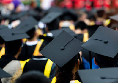 Image of graduates in their caps and gowns sitting at a graduation ceremony.