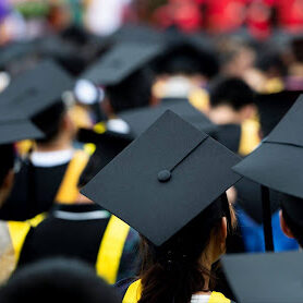 Image of graduates in their caps and gowns sitting at a graduation ceremony.
